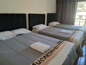A hotel room with three beds, each with a headboard and pillows.