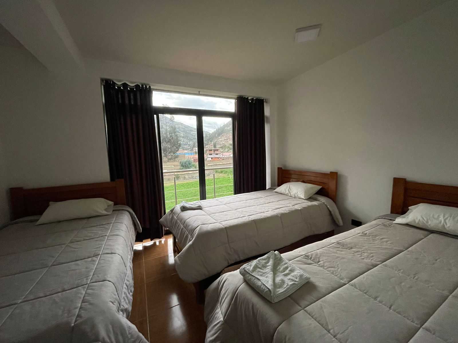 A hotel room with two beds, a large window, and a view of a green landscape.
