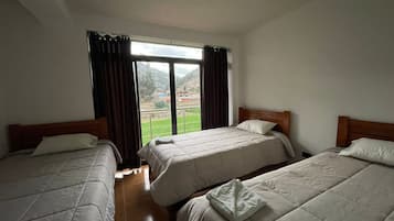 A hotel room with two beds, a large window, and a view of a green landscape.