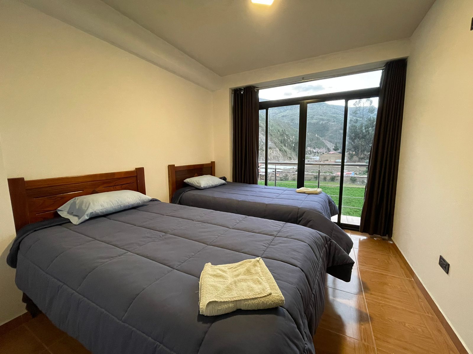 A hotel room with two beds, a large window with a view of a mountainous landscape, and a wooden floor.