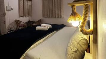 Quarto com cama, luminária, cadeira e mesa pequena.
