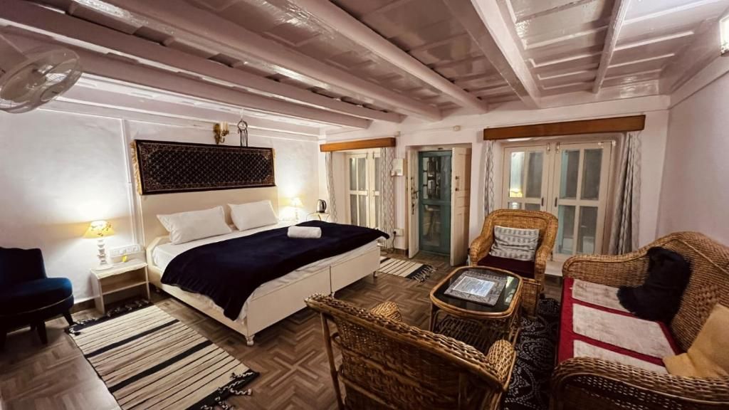 Un dormitorio con una cama, mesitas de noche, una silla, una pequeña mesa y una puerta.