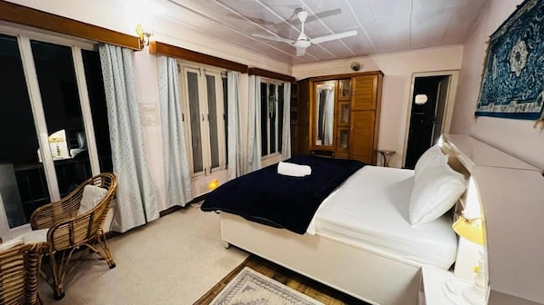 Un dormitorio con una cama, una silla, un ventilador de techo y una ventana con cortinas.