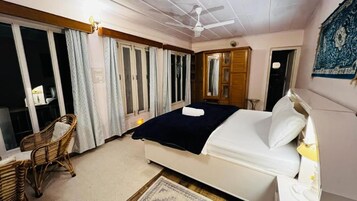 Un dormitorio con una cama, una silla, un ventilador de techo y una ventana con cortinas.