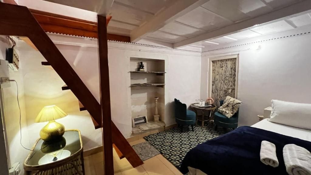 A hotel room with a bed, a chair, a small table with a lamp, a wardrobe, and a window with curtains.