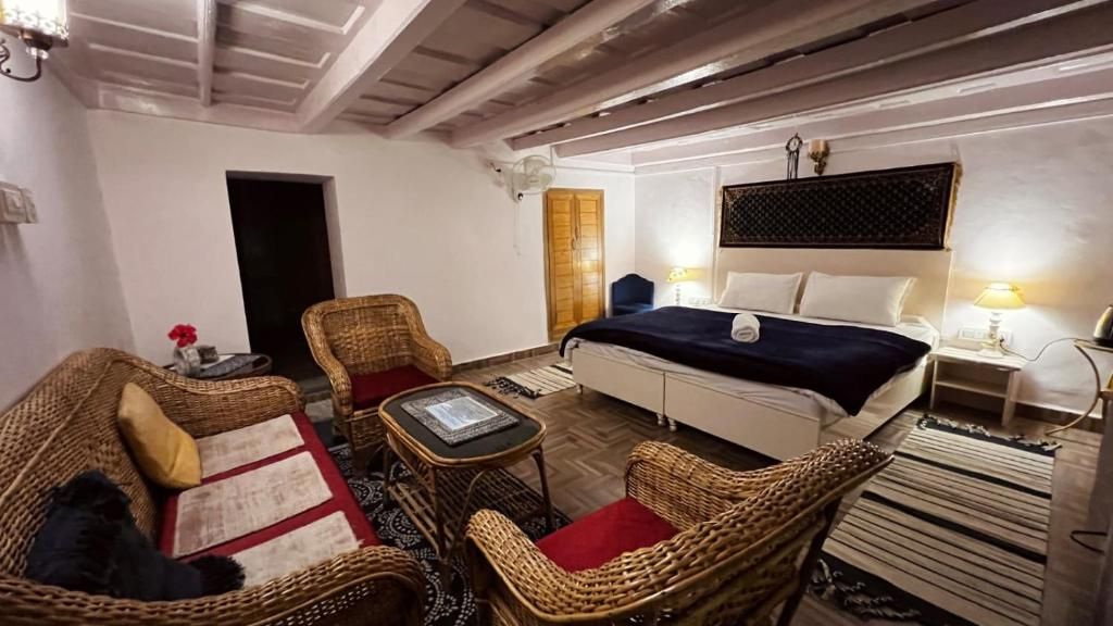 A cozy room with a bed, two wicker chairs, a small table, and a nightstand with lamps.