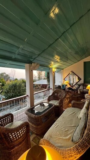 Un espacio de estar techado al aire libre con mobiliario de mimbre y una mesa, con vistas a un jardín.
