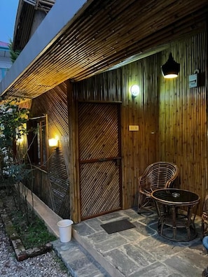 A wooden exterior with a bamboo wall, a glass door, and a seating area with wicker chairs and a table.