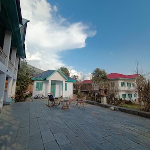 A paved courtyard with a building featuring a green door and windows, a bicycle, and a rocking chair. - Moonshine Villa (Bir)