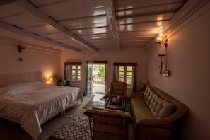 A bedroom with a bed, a sofa, a chair, and a small table. There are two doors leading to an outdoor area. - Moonshine Villa (Bir)