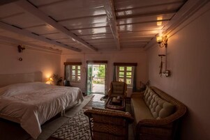 Un dormitorio con cama, sofá, sillón y una mesita. Dos puertas dan acceso a un espacio exterior.