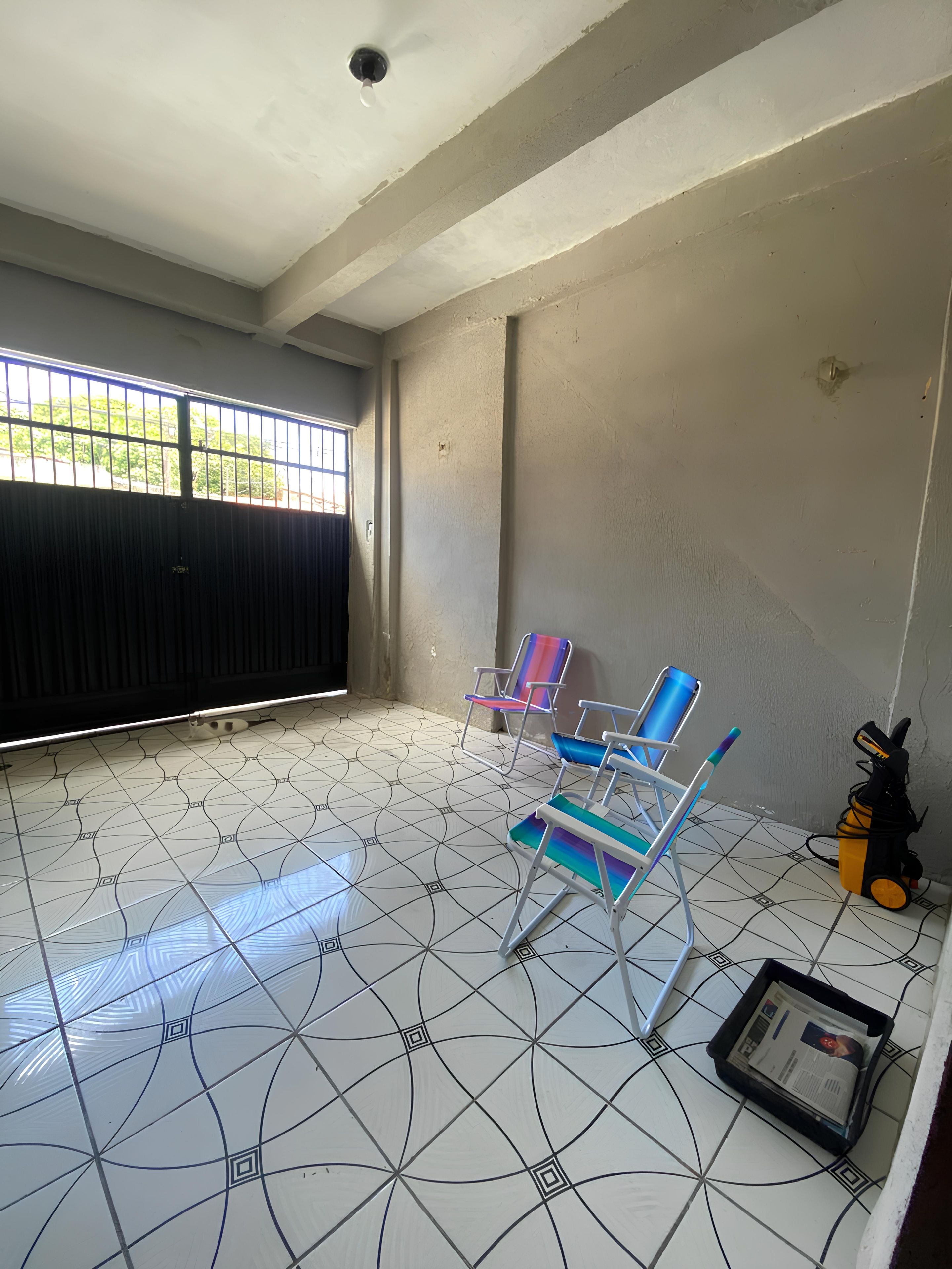 Um quarto com piso de azulejos, uma janela com grades e duas cadeiras coloridas.