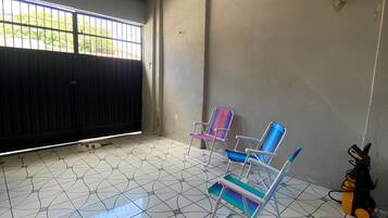 Um quarto com piso de azulejos, uma janela com grades e duas cadeiras coloridas.