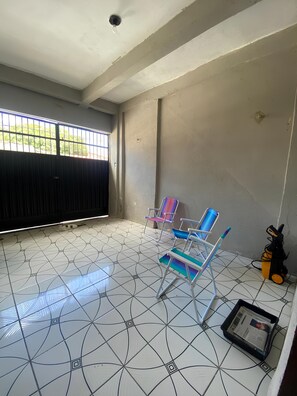 Um quarto com piso de azulejos, uma janela com grades e duas cadeiras coloridas.