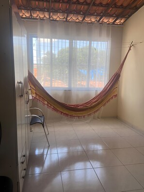 Habitació amb un bressol, una cadira i una finestra gran.