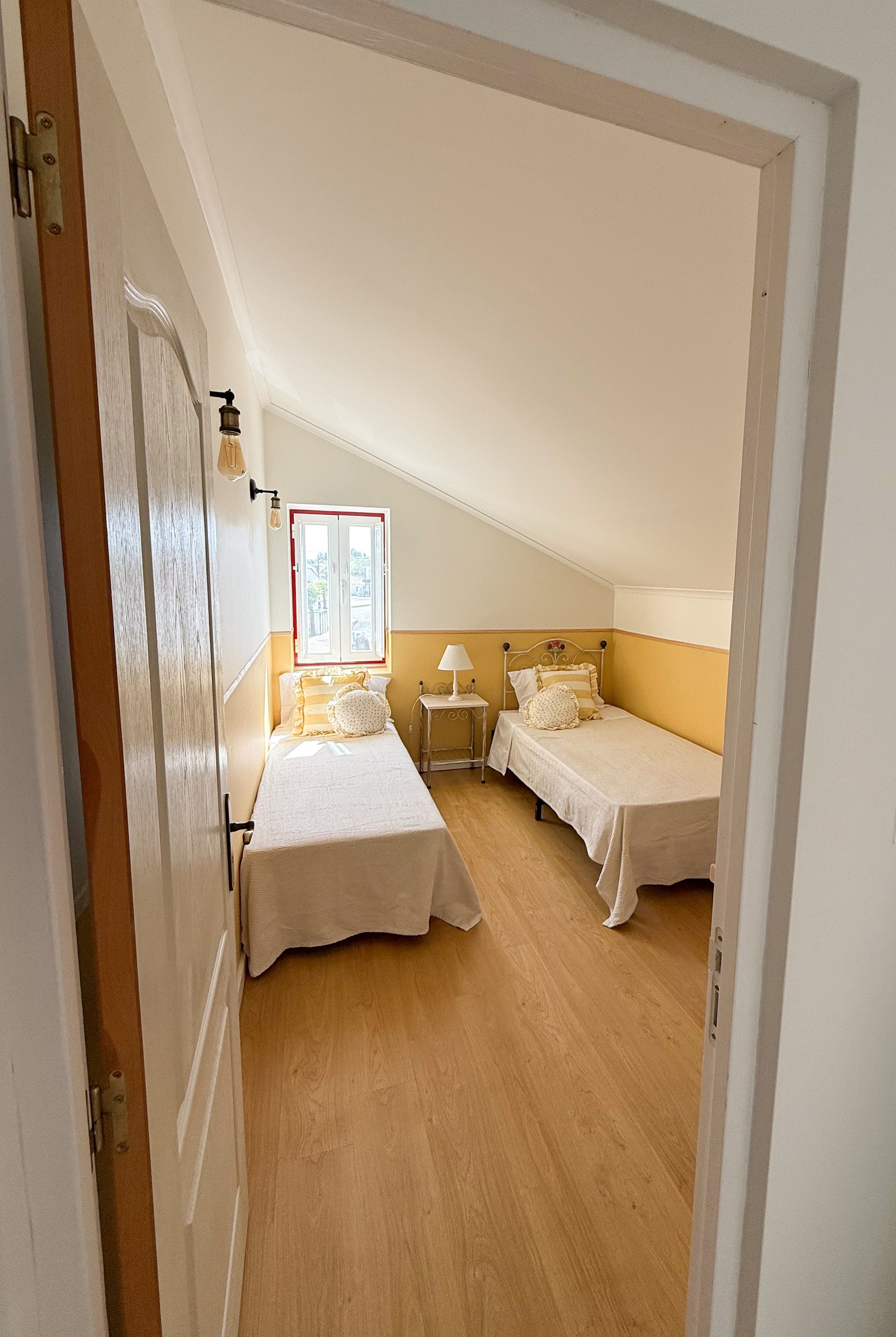 Un dormitorio con dos camas individuales, una mesita de noche, una lámpara y una ventana con vistas.