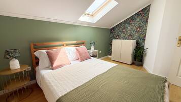 Quarto com cama, claraboia, guarda-roupa, mesa de cabeceira, abajur e planta em vaso.