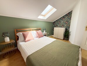 Un dormitorio con cama, tragaluz, armario, mesita de noche, lámpara y planta en maceta.