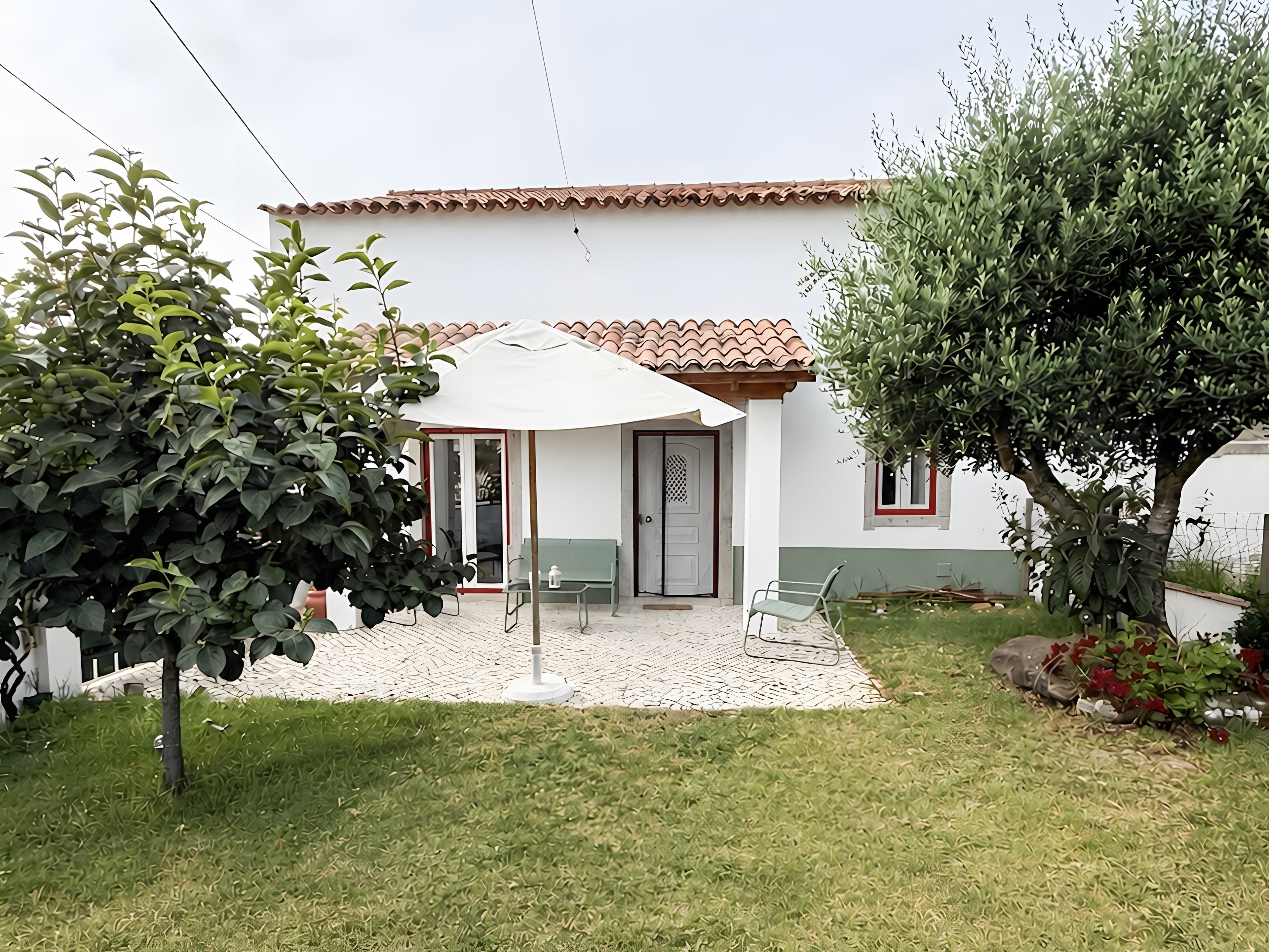 Una casa con techo de tejas, un porche cubierto con una banca y un pequeño jardín.