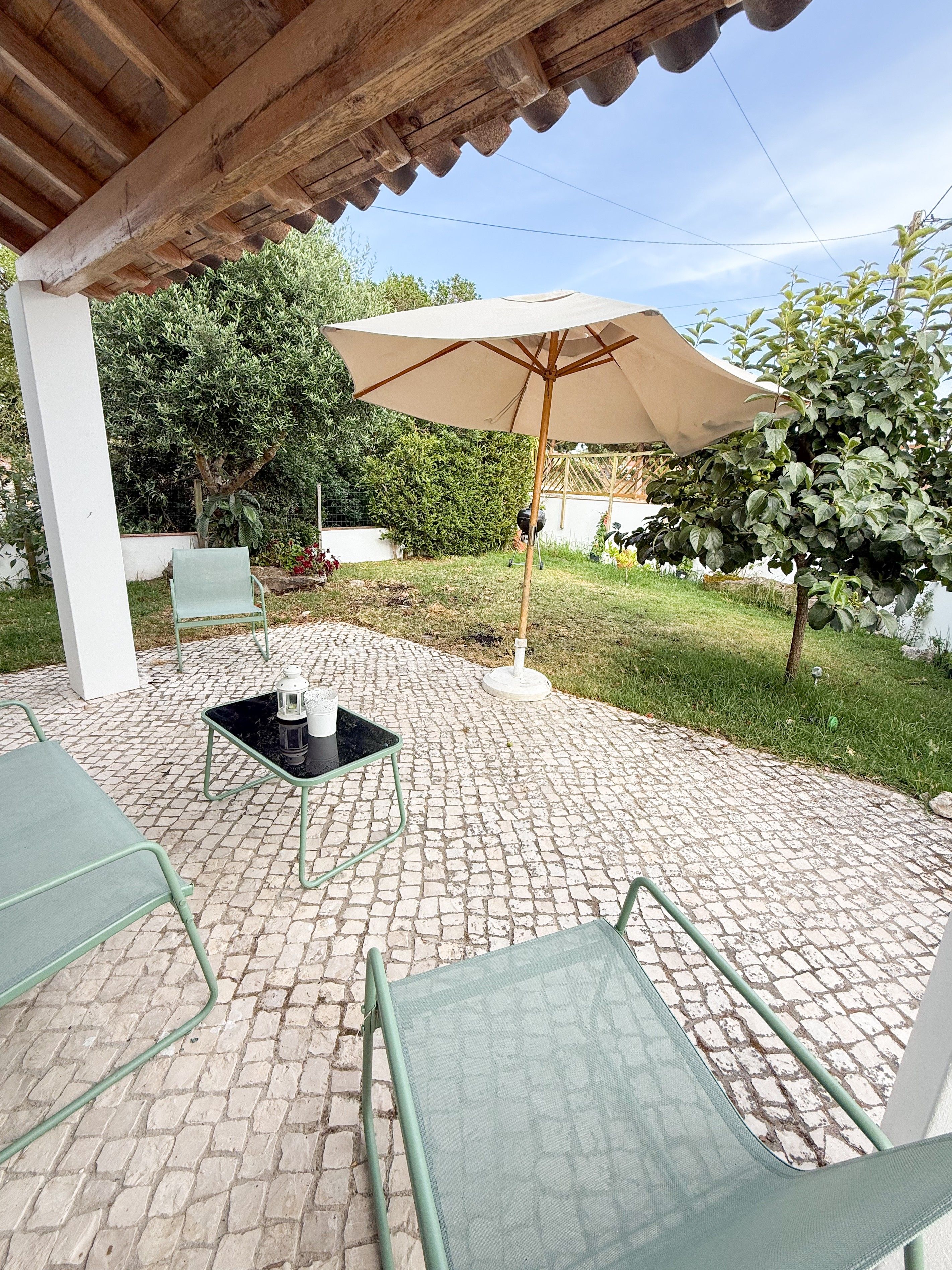 Een buitenterras met een tafel en stoelen, een pergola erboven en een grote parasol voor schaduw.