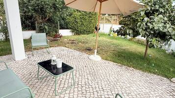 Een buitenterras met een tafel en stoelen, een pergola erboven en een grote parasol voor schaduw.