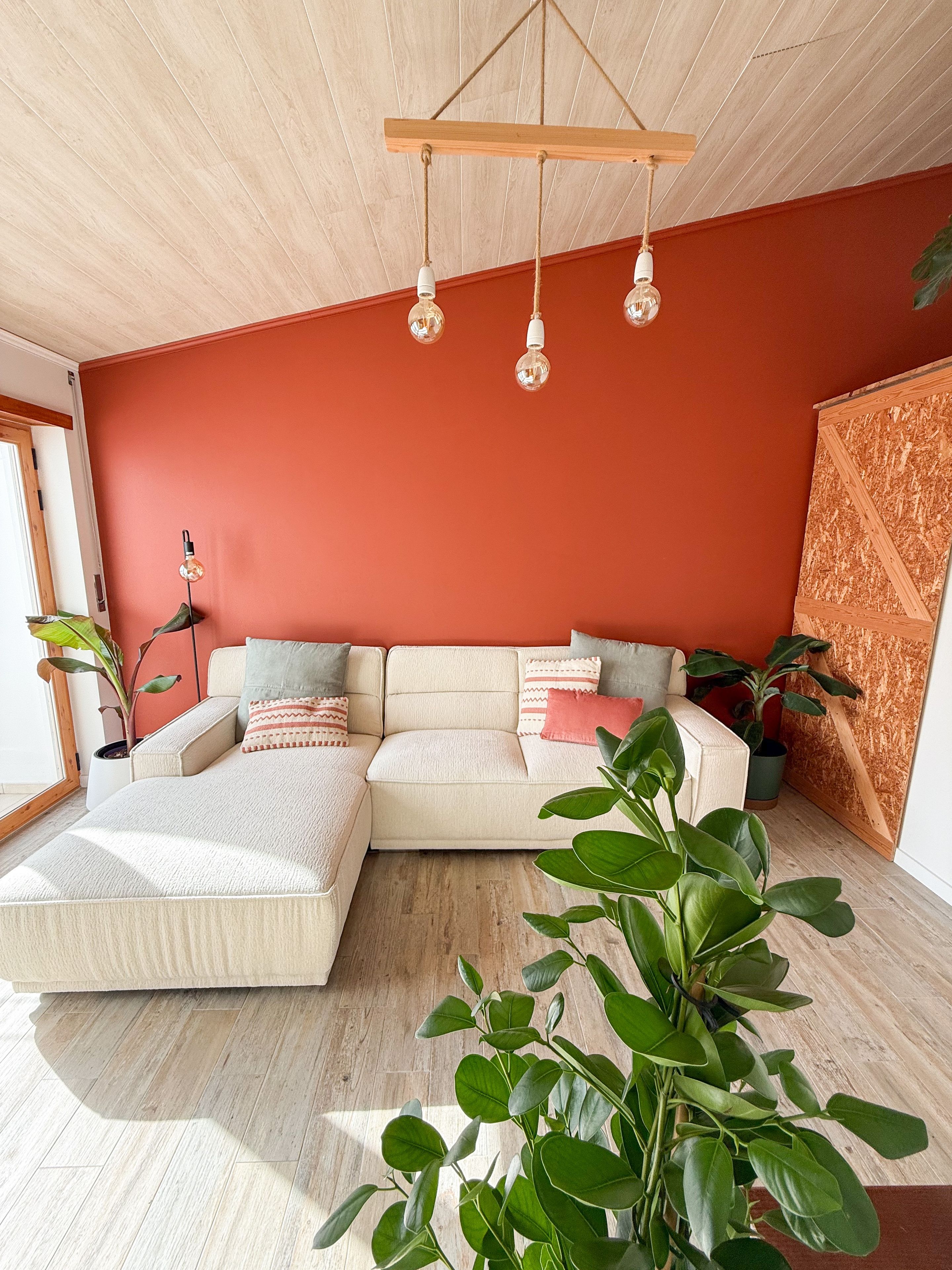 Ein modernes Wohnzimmer mit einer Eckcouch, einer Hängeleuchte und einer großen Pflanze.