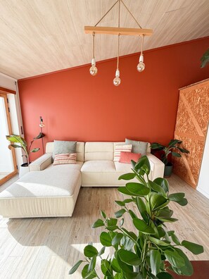 Ein modernes Wohnzimmer mit einer Eckcouch, einer Hängeleuchte und einer großen Pflanze.