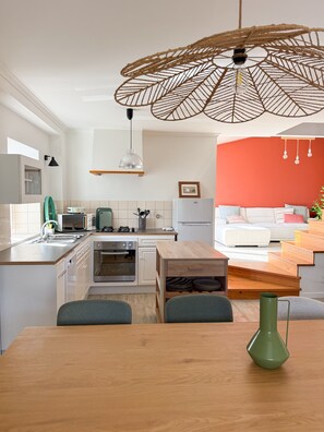 Una cocina moderna con armarios blancos, una mesa de comedor de madera y un jarrón verde.