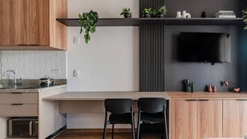 Uma cozinha moderna com bancada de madeira, duas cadeiras pretas, forno embutido e uma TV de tela plana na parede.