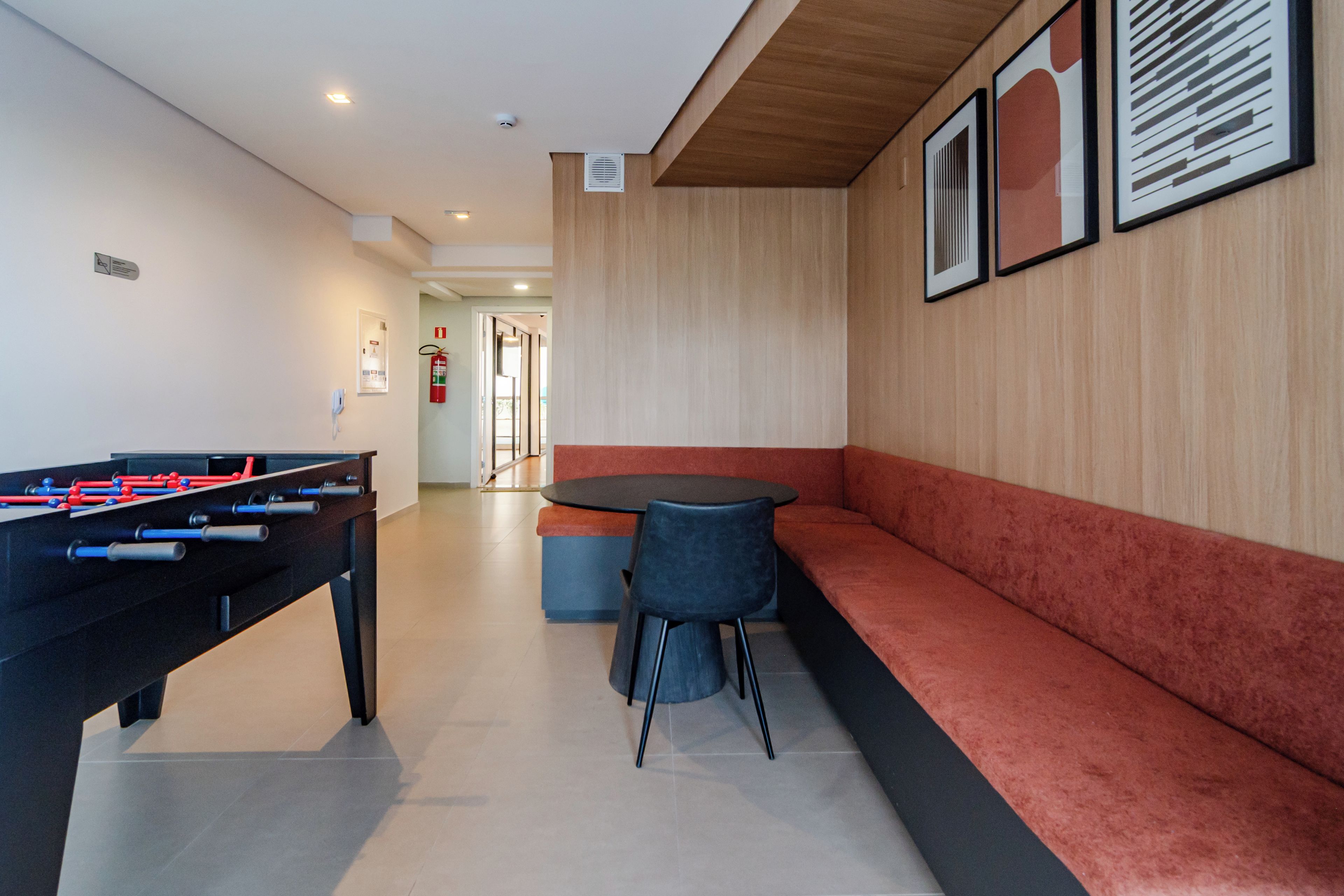 Una habitación con mesa de fútbolín, un sofá y una mesa con sillas. Hay una puerta que conduce a otra habitación.