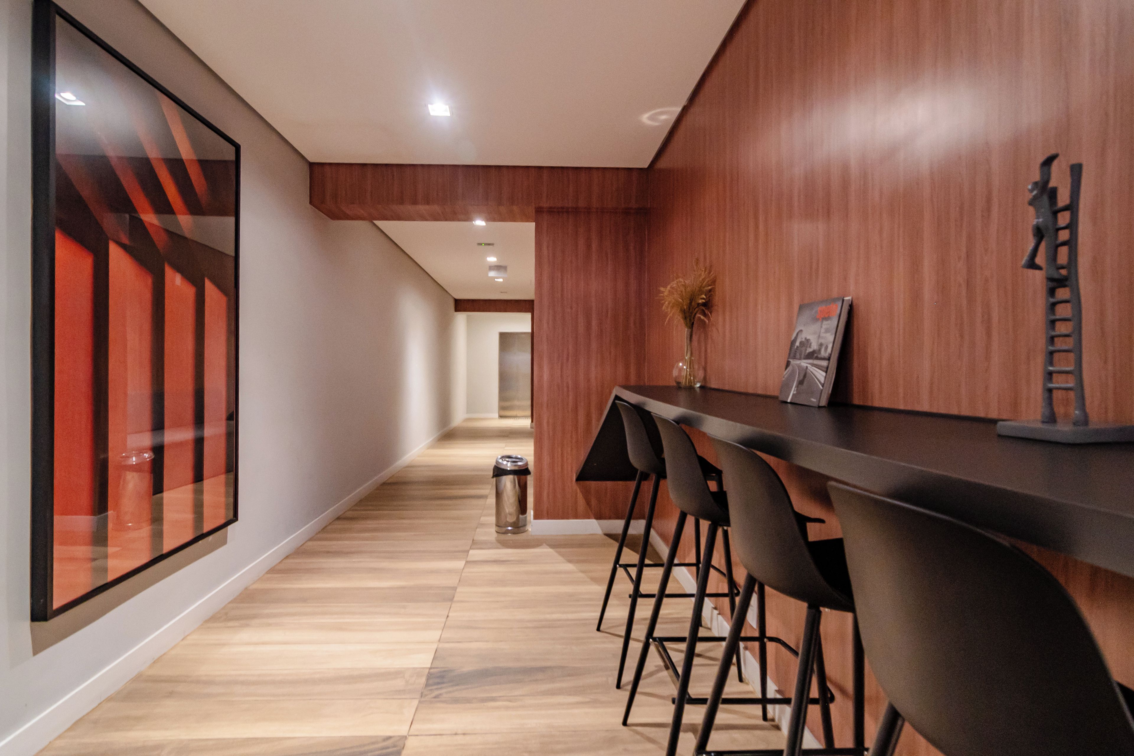 Un interior moderno con un largo pasillo, paneles de madera, una zona de bar con taburetes y un basurero.