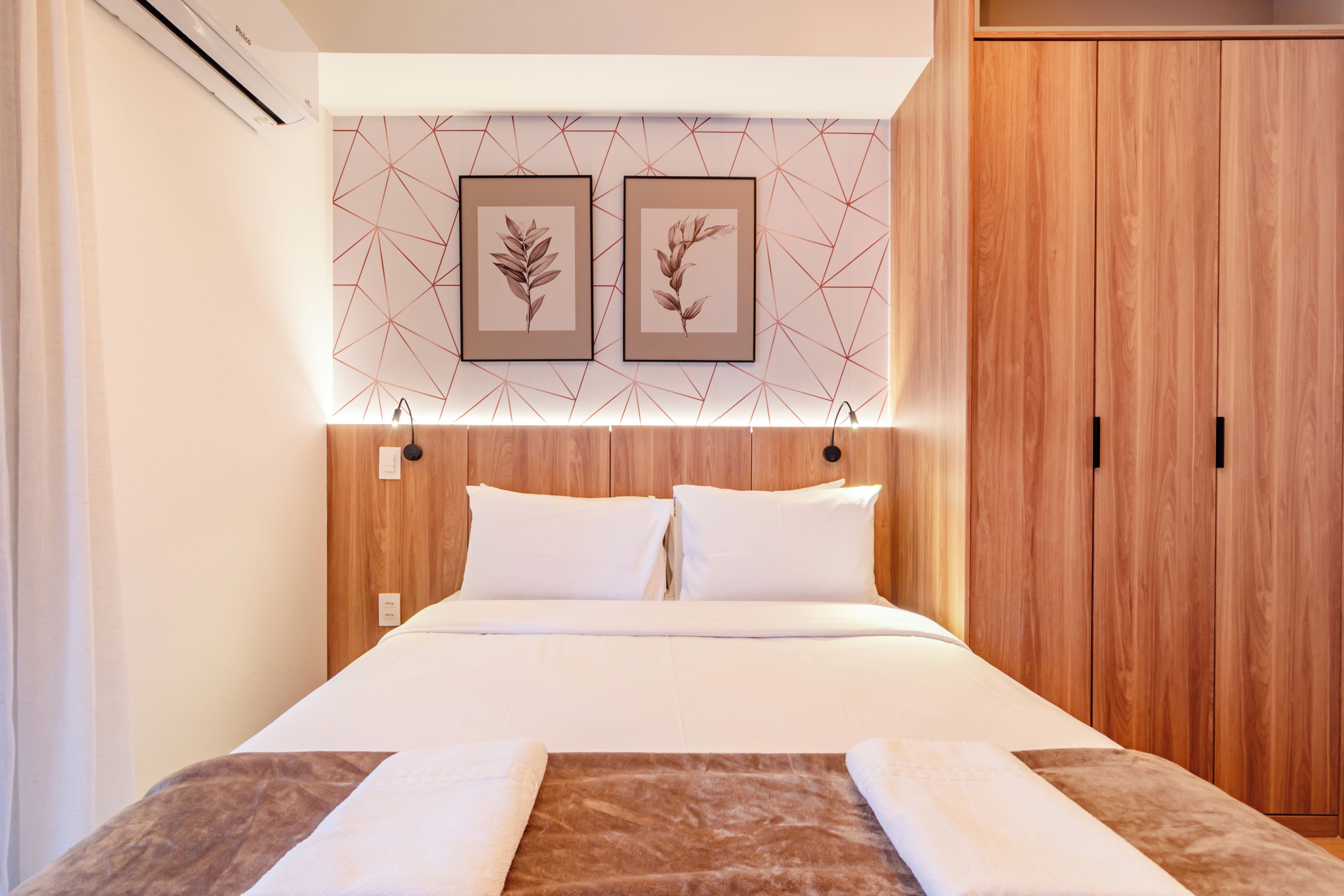 Habitación de hotel con cama, cabecera de madera, dos cuadros enmarcados y un armario.