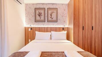 Habitación de hotel con cama, cabecera de madera, dos cuadros enmarcados y un armario.