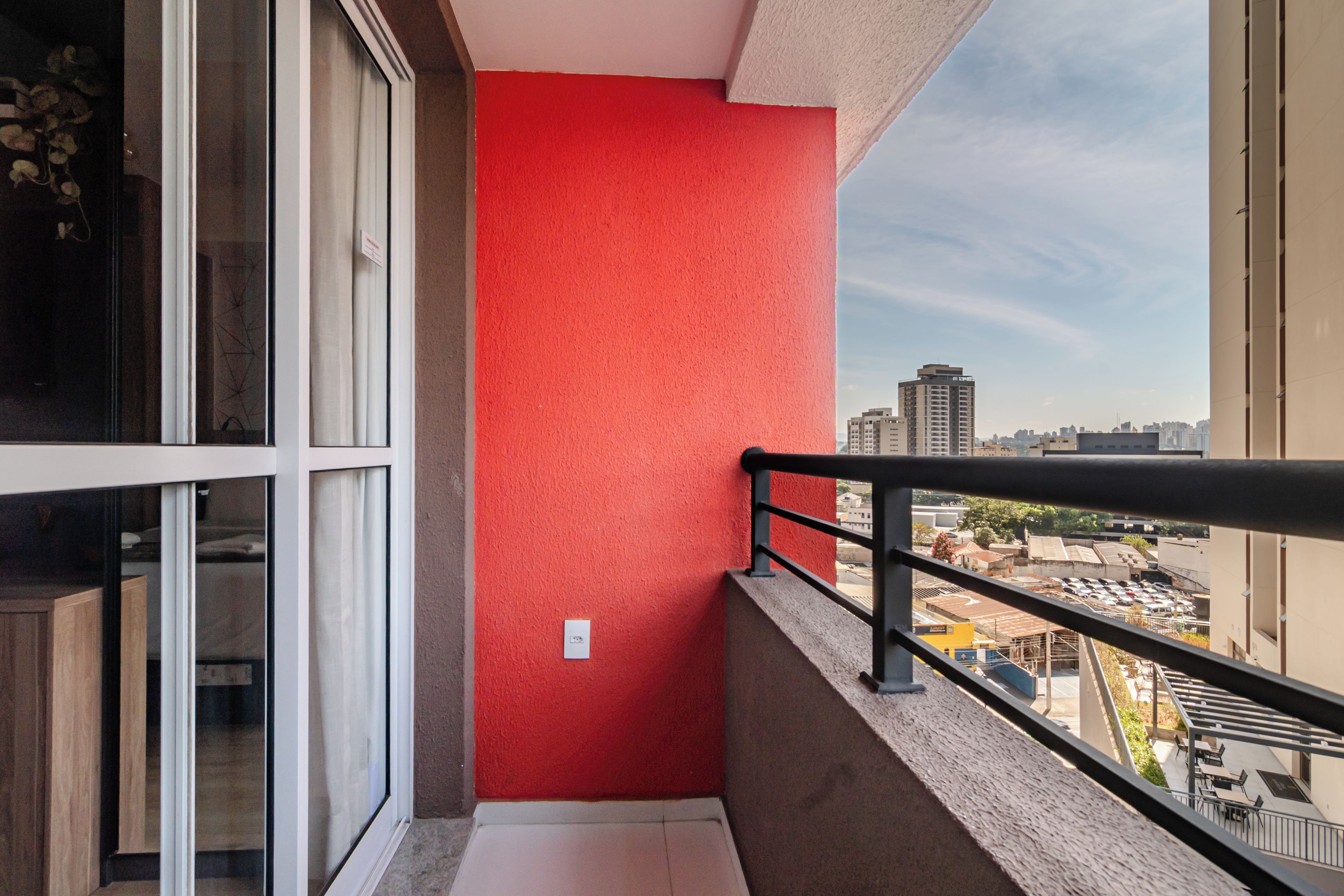 Un balcón con pared roja, puerta de cristal y vista a la ciudad.