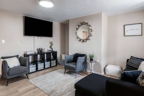 A living room with a flat-screen TV, a sofa, a coffee table, and a decorative mirror. - Summit Row | Both Houses (Pittsburgh)