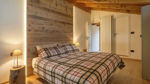 A bedroom with a wooden ceiling, a bed with a plaid bedspread, two bedside lamps, and a door leading to another room. - Casa Quaranta - Two Bedroom Apartment, Sleeps 4 (Ponte di legno)