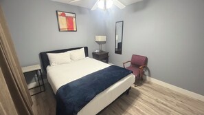 A hotel room with a bed, bedside table, lamp, chair, and artwork on the wall.