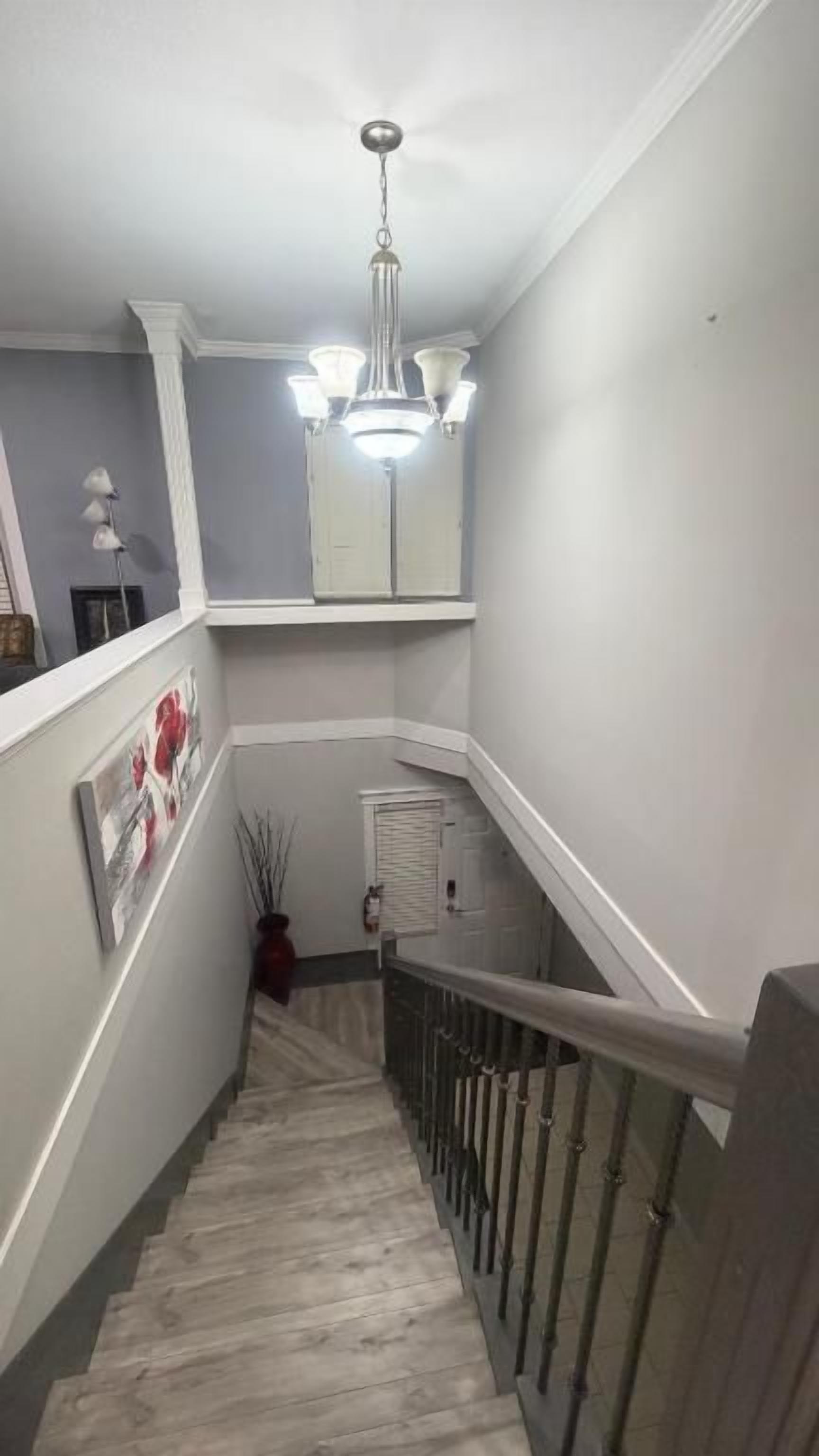 Una escalera estrecha con barandilla, una lámpara arriba y una puerta al final.