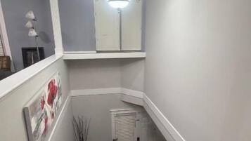 Una escalera estrecha con barandilla, una lámpara arriba y una puerta al final.