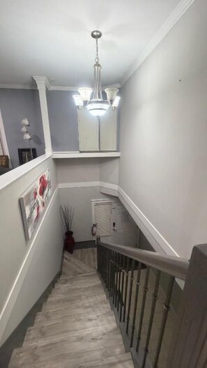 A narrow staircase with a handrail, a light fixture above, and a door at the bottom.