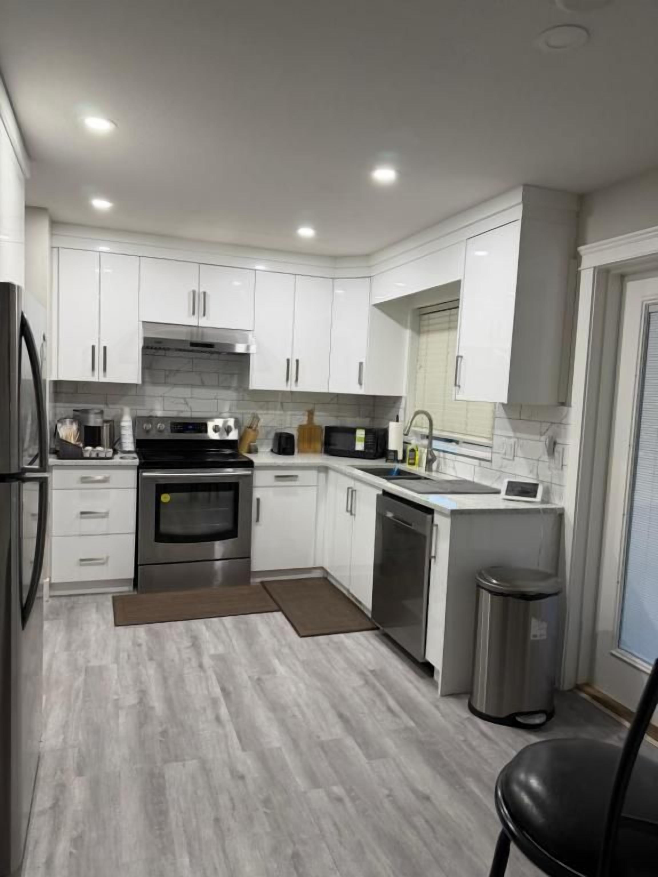 A modern kitchen with white cabinets, stainless steel appliances, and a grey floor.