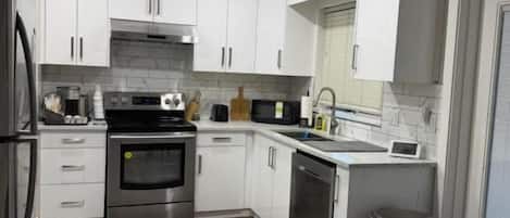 Una cocina moderna con armarios blancos, electrodomésticos de acero inoxidable y piso gris.