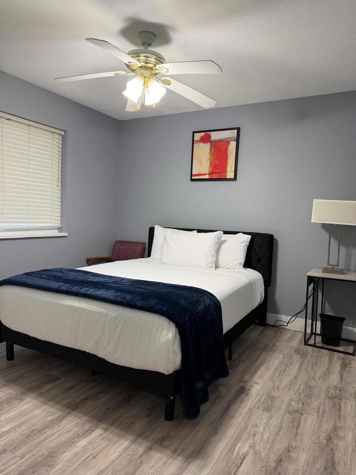 Un dormitorio con cama, ventilador de techo, lámpara de pared y ventana con persianas.