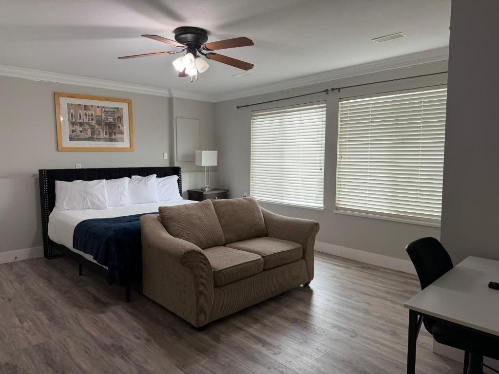 A bedroom with a bed, a sofa, a ceiling fan, and large windows with blinds.