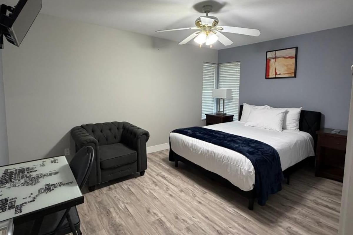 A bedroom with a bed, a ceiling fan, a desk, and a chair.
