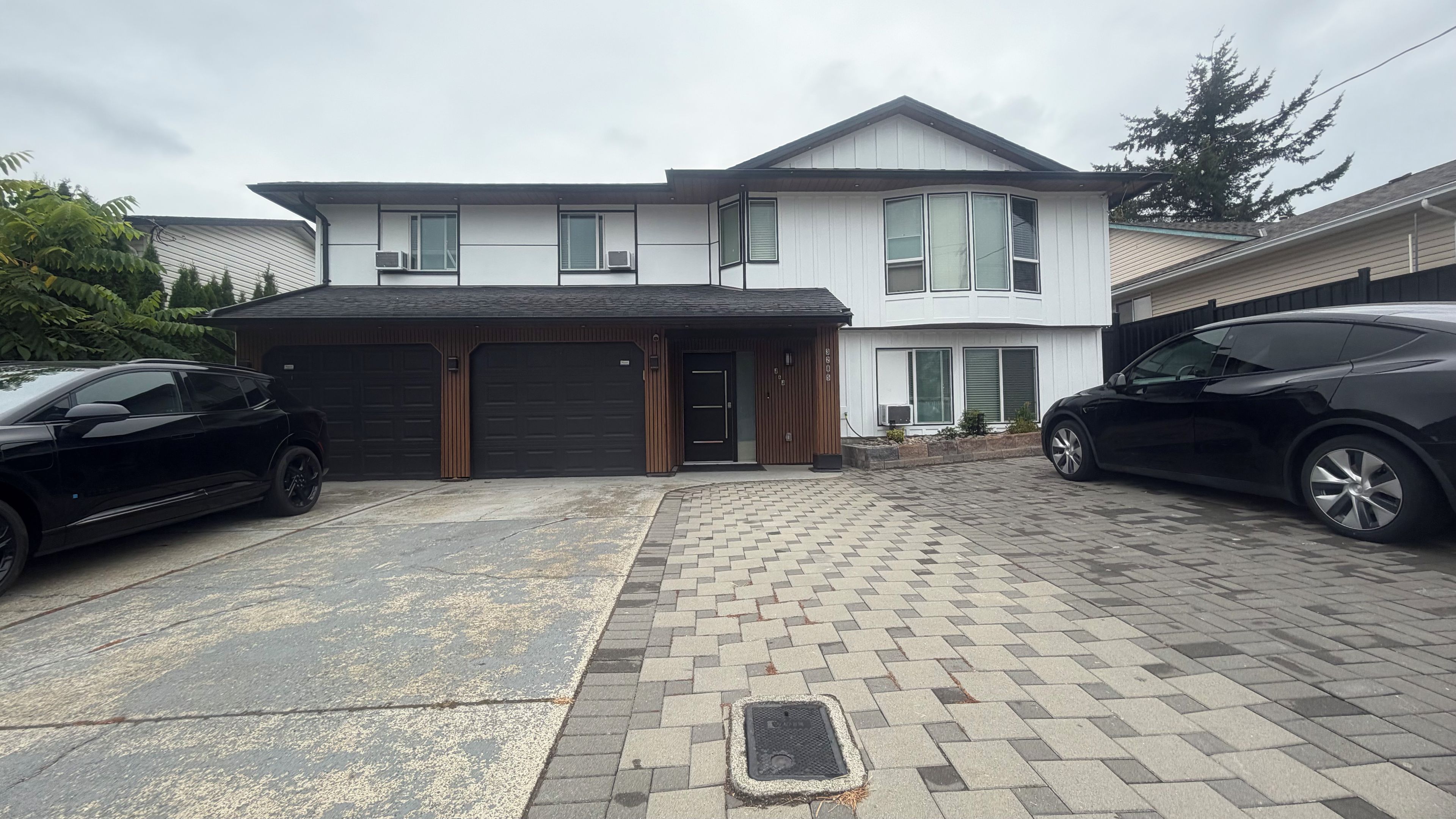 A two-story residential building with a garage, paved driveway, and a small front yard.