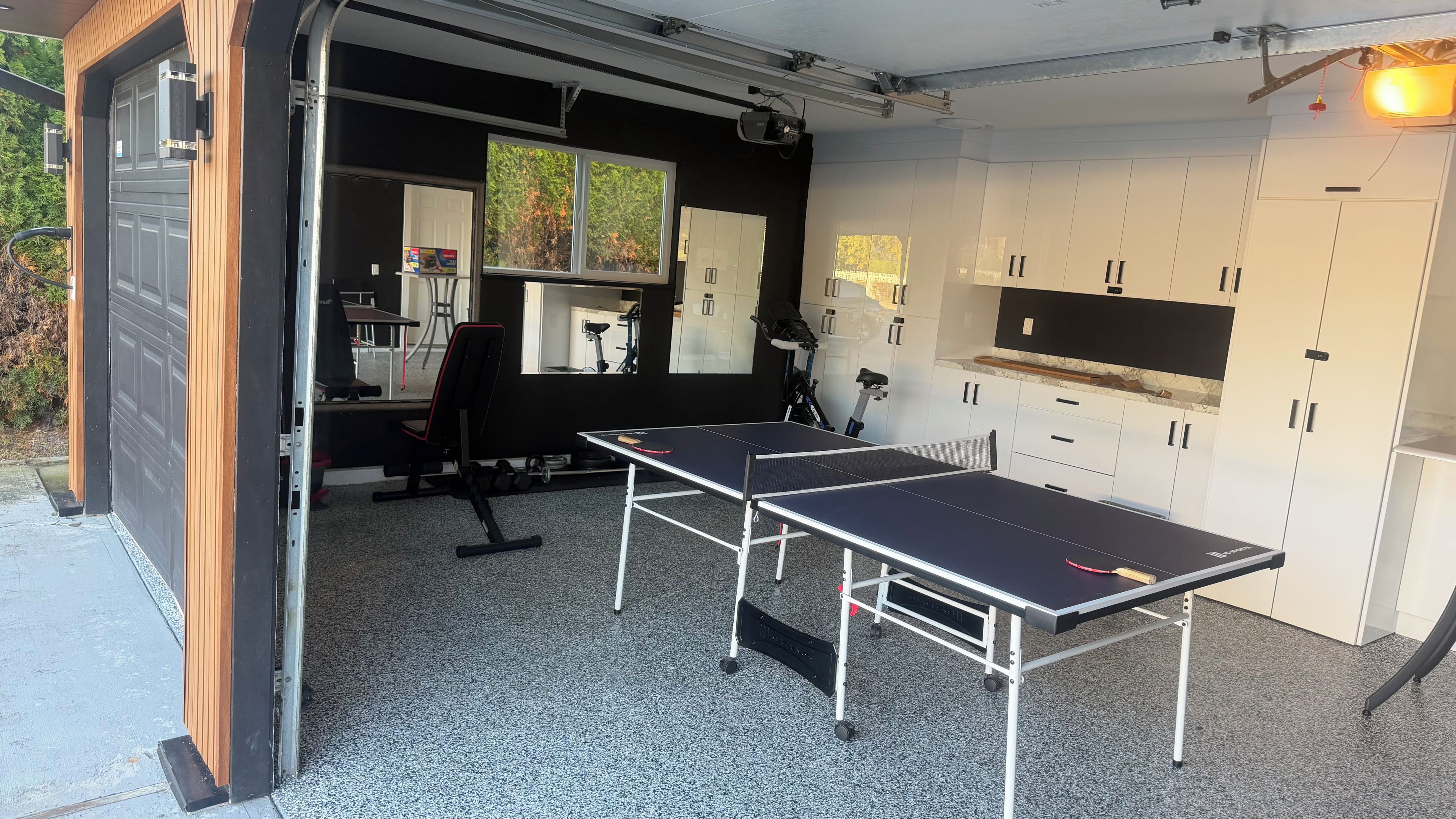 Un garaje con mesa de ping pong, equipo de ejercicio y un proyector.