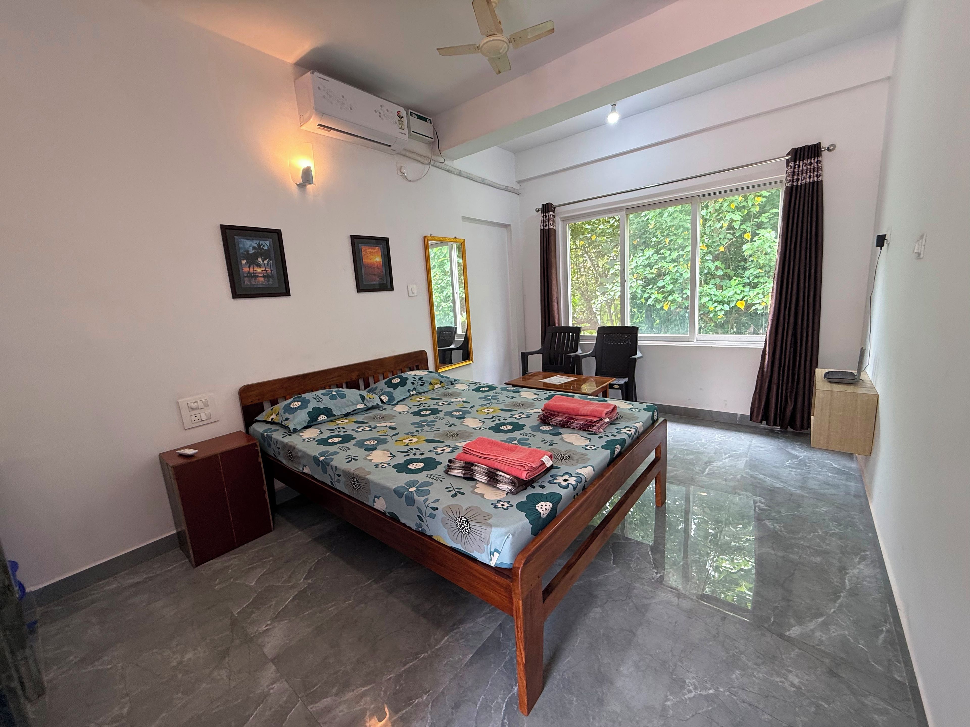 A bedroom with a bed, a desk, a chair, a window with curtains, and an air conditioning unit.