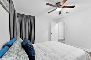 Ein Schlafzimmer mit Bett, Deckenventilator und einer Tür zu einem weiteren Raum.