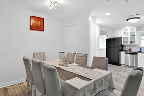 A modern kitchen with white cabinets, a black refrigerator, and a dining area with a table set for six. - Near AT&T Stadium | Parking | Pets OK (Arlington)